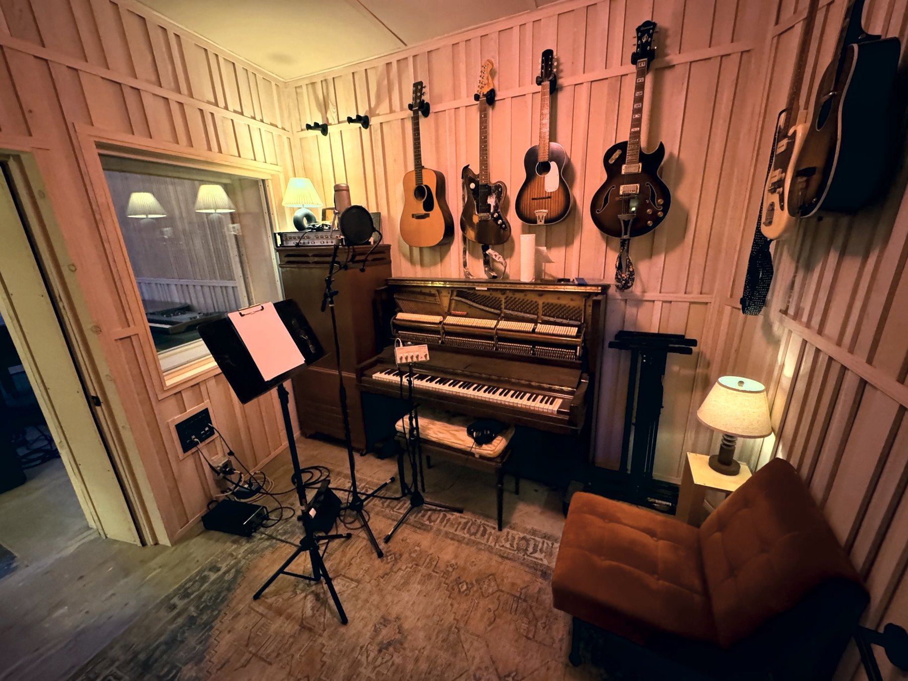 Booth with upright piano, hanging guitars and a vocal mic